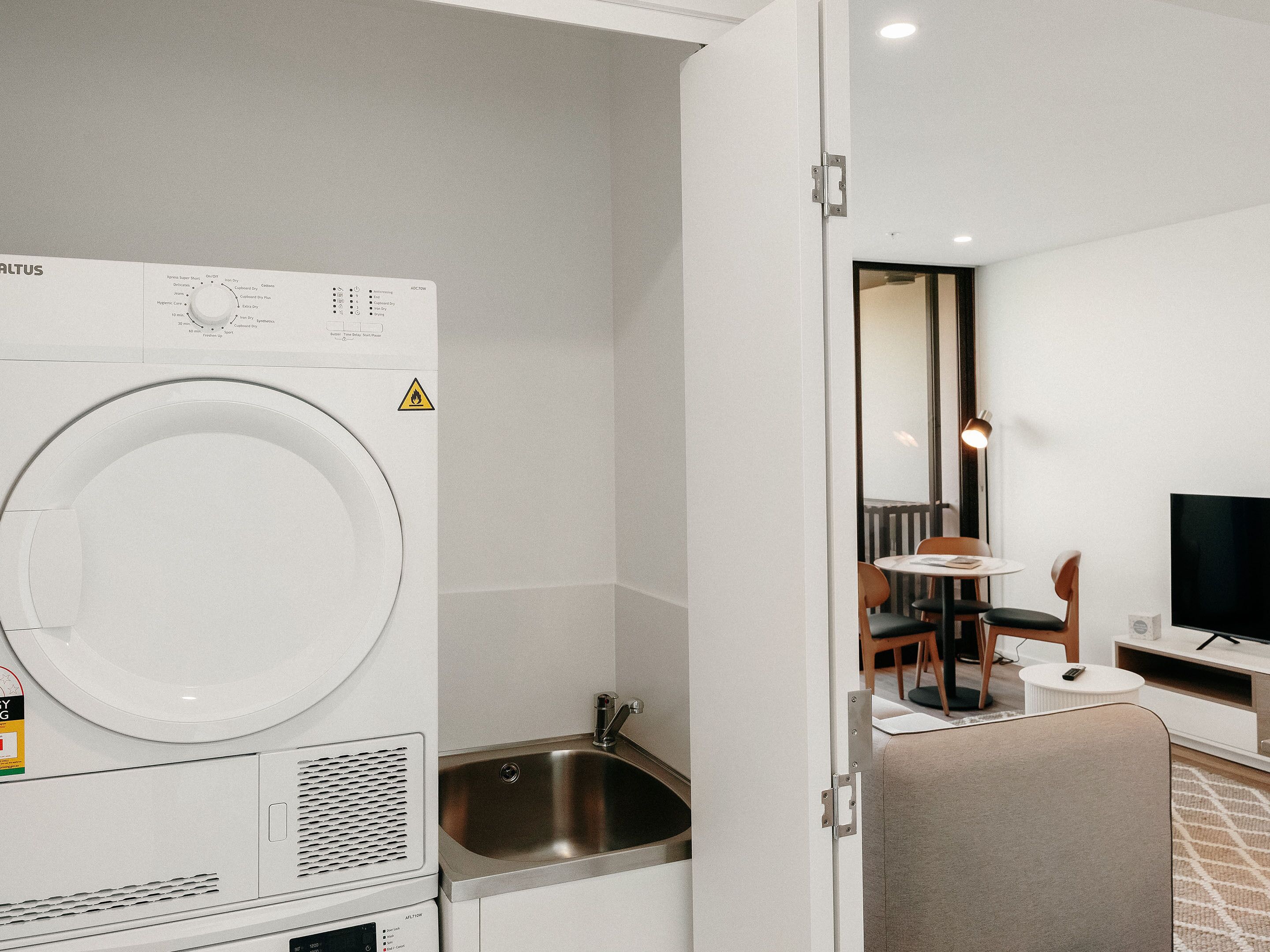 Une chambre d’hôtel compacte équipée d’un lave-linge, d’un évier, d’une petite table avec une chaise et d’un téléviseur.
