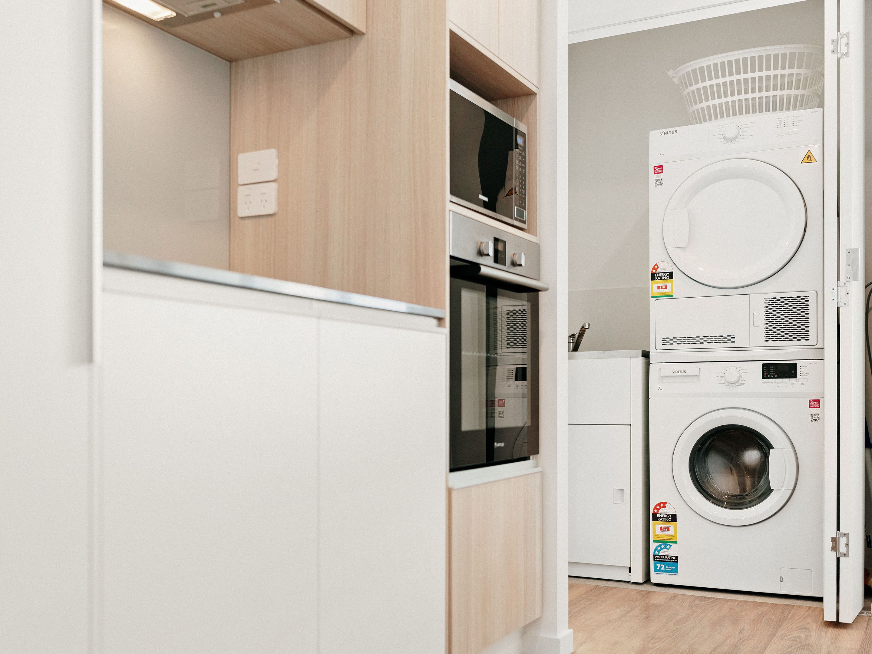 A compact laundry room with a washing machine and dryer, wooden cabinetry, and a microwave.