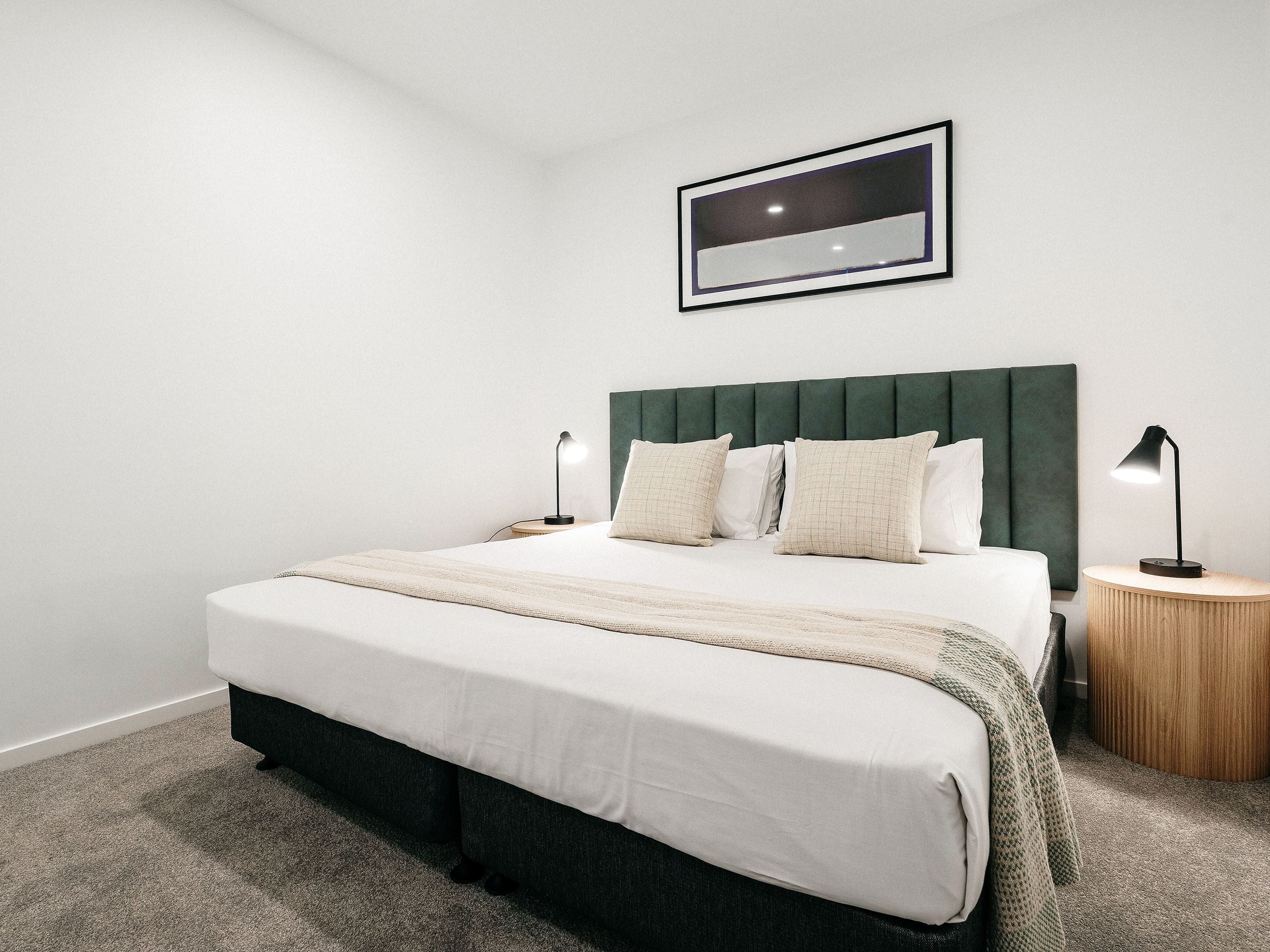 A neatly arranged bedroom with a large bed, two bedside tables, a headboard, and a framed picture on the wall.