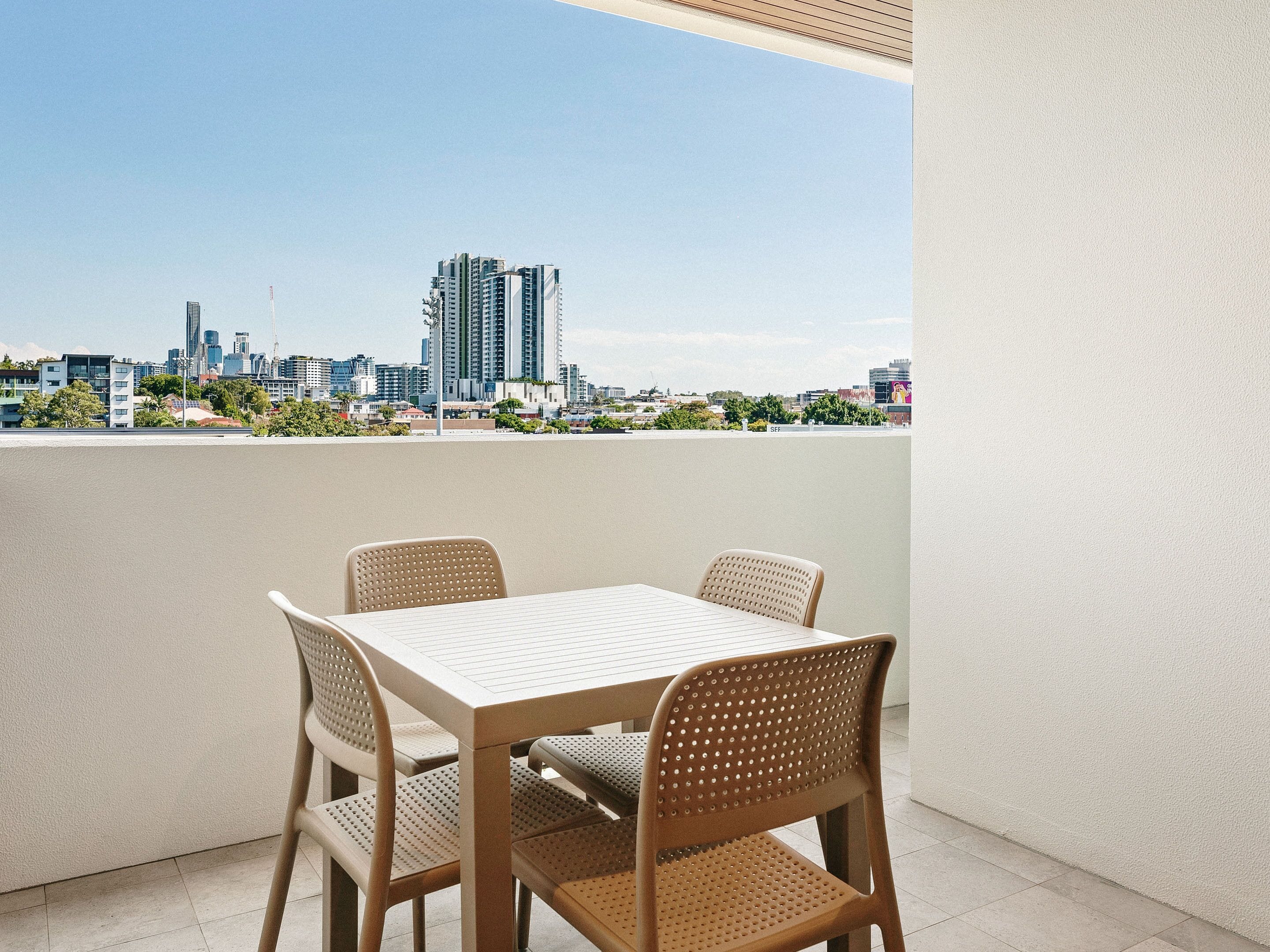 A balcony with a table and chairs, overlooking a cityscape with modern buildings.