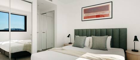 Un dormitorio moderno con una cama grande, un cabecero tapizado en verde y vistas a través de una ventana.