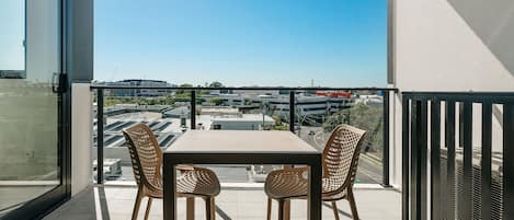 A balcony with a table and chairs, offering a view of a parking lot and buildings.