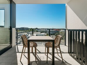Un balcon avec une table et des chaises, d’où l’on peut admirer un parking et des immeubles.
