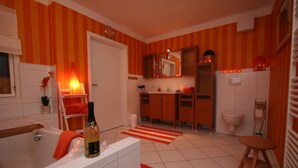 A modern bathroom with a bathtub, a sink, and a toilet. There is a red and white striped rug on the floor. - Eckhorst Farm, Tuscany (Güby)