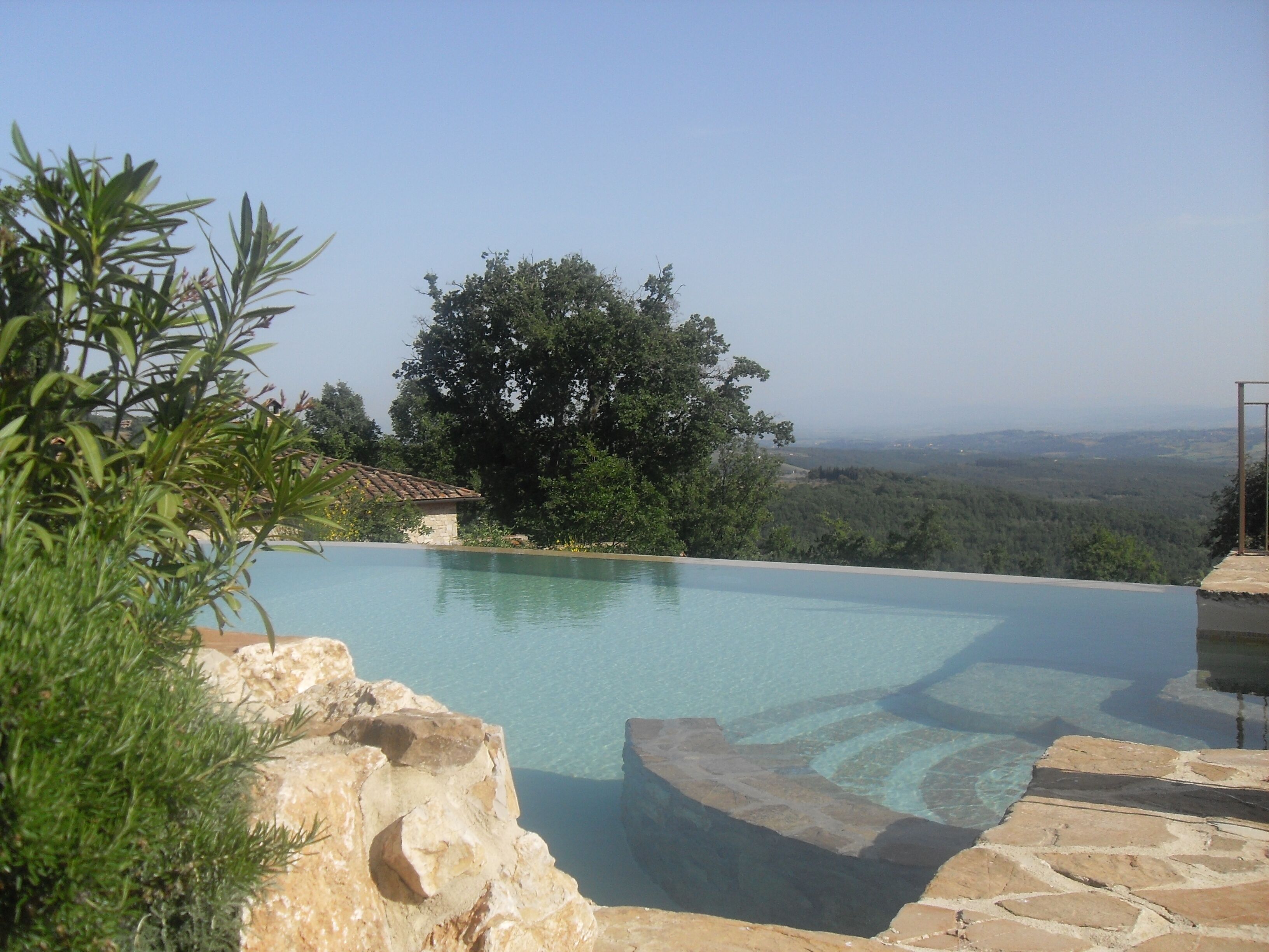 A clear infinity pool with a view of a forested landscape and distant hills.