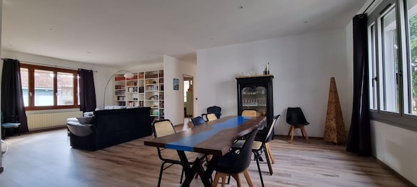 A spacious living area with a wooden dining table, black chairs, a sofa, a bookshelf, and a fireplace.