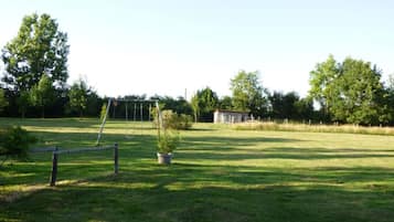 A grassy field with a swing set, a small shed, and a fenced area.