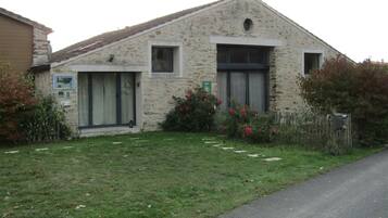 A stone building with a sloped roof, a small porch, and a garden with red flowers.