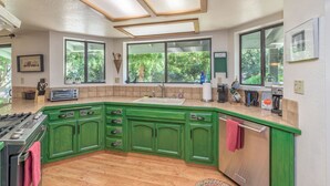 Une cuisine moderne avec des meubles de couleur verte, une grande fenêtre et une cuisinière encastrée.
