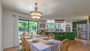 Un coin repas avec une table dressée pour quatre personnes, des chaises en bois, un lustre et une vue sur l’extérieur.