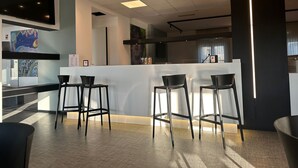 Zona de bar moderna con un mostrador blanco, taburetes negros y un techo con iluminación empotrada.
