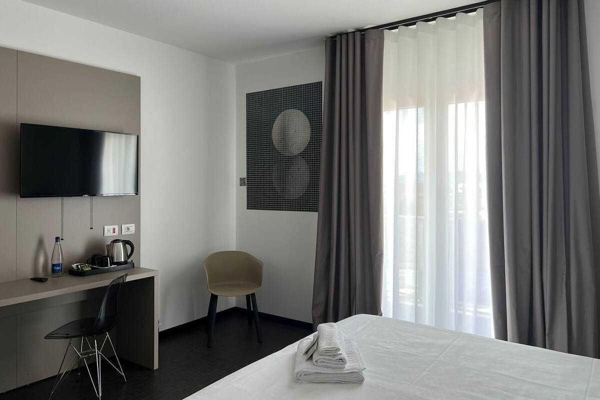 Ein Hotelzimmer mit einem Bett, einem Schreibtisch mit Stuhl, einem Fernseher und einem Fenster mit Vorhängen.