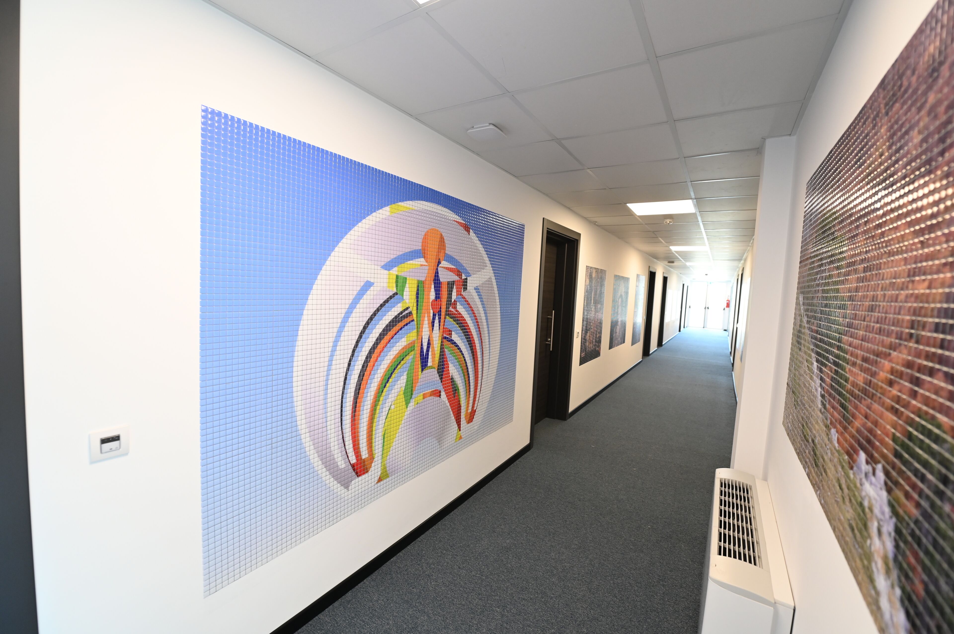 Un pasillo con un mural abstracto y colorido en la pared izquierda, una unidad de ventilación a la derecha y puertas que dan a varias habitaciones.