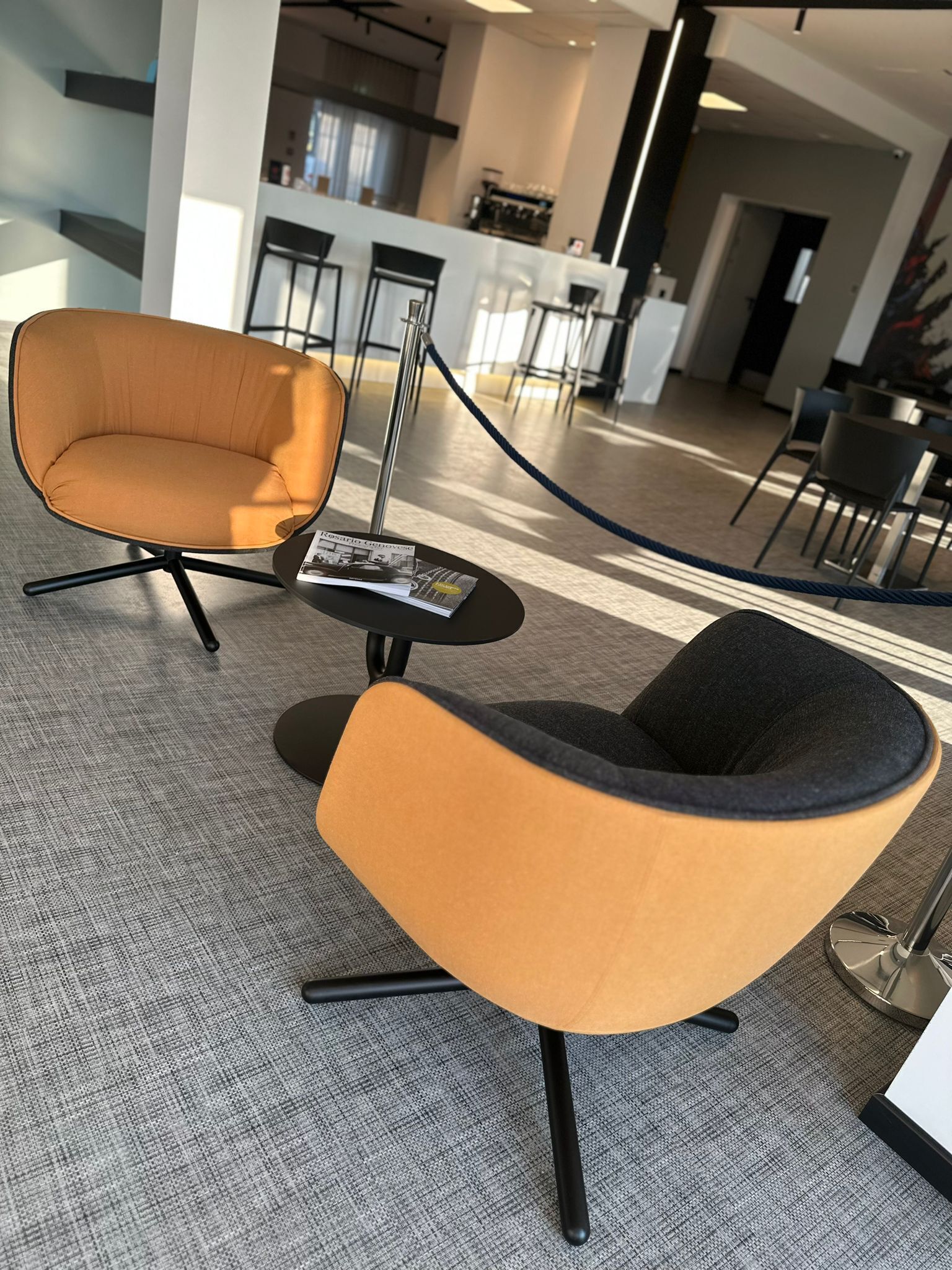A modern office space with a high chair and a small table, both featuring black metal legs and a combination of black and orange upholstery.