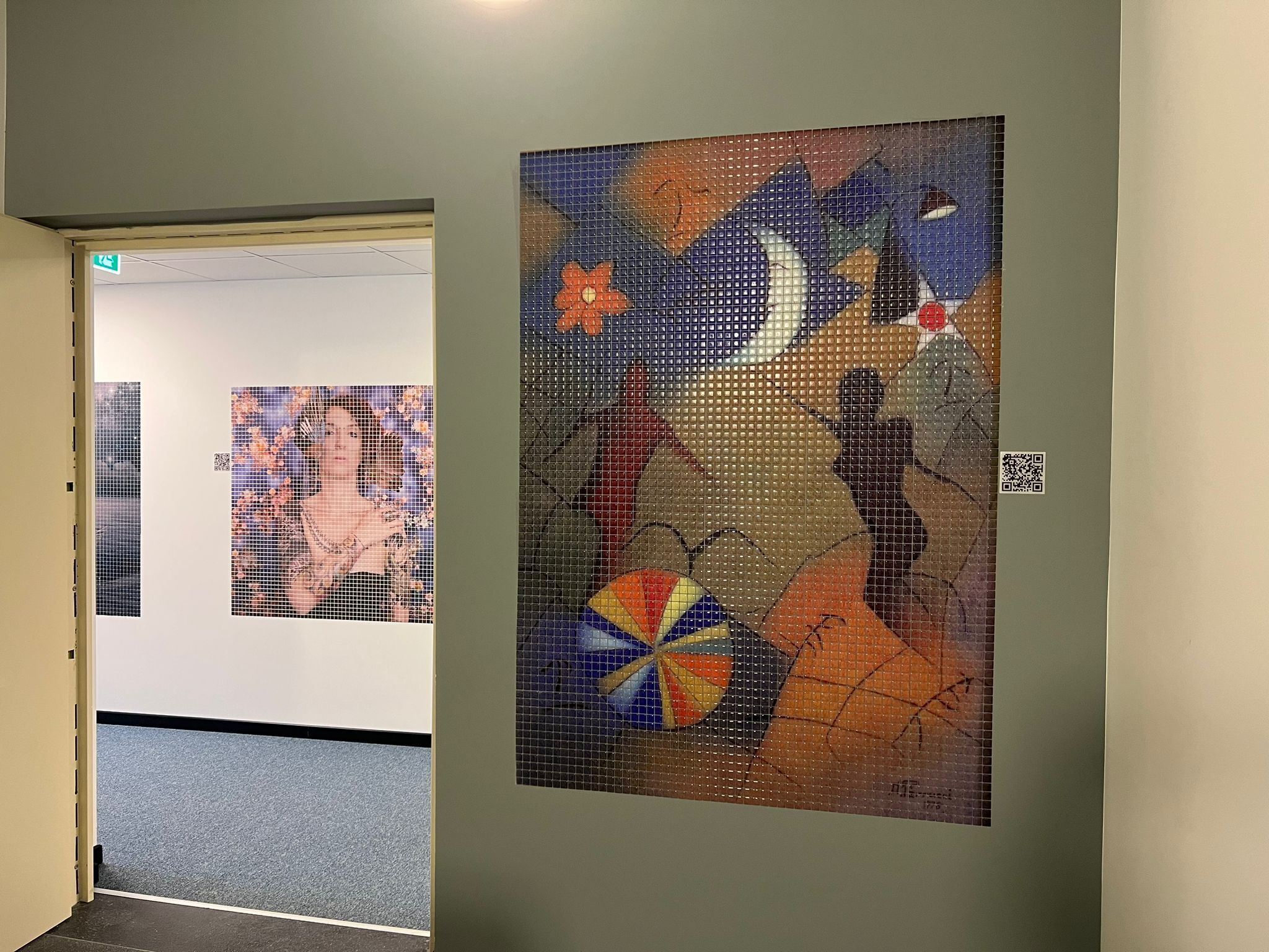 A hallway with two artworks on the walls, a door, and a carpeted floor.