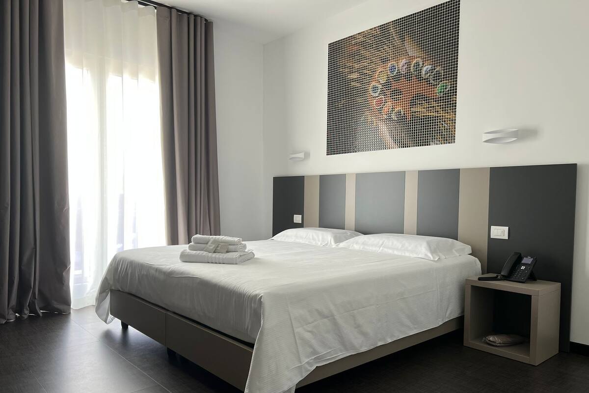 Ein modernes Hotelzimmer mit einem großen Bett, einem Nachttisch mit Telefon und einem an der Wand hängenden Kunstwerk.