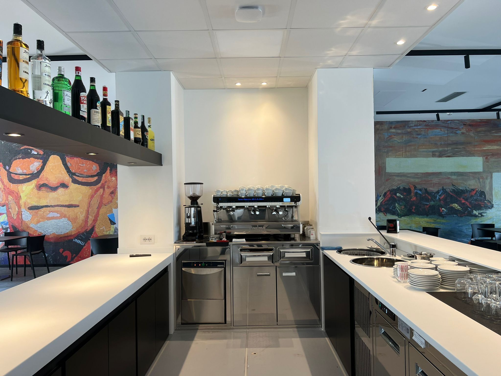 A modern bar area with a coffee machine, shelves with liquor bottles, and a large digital art display.