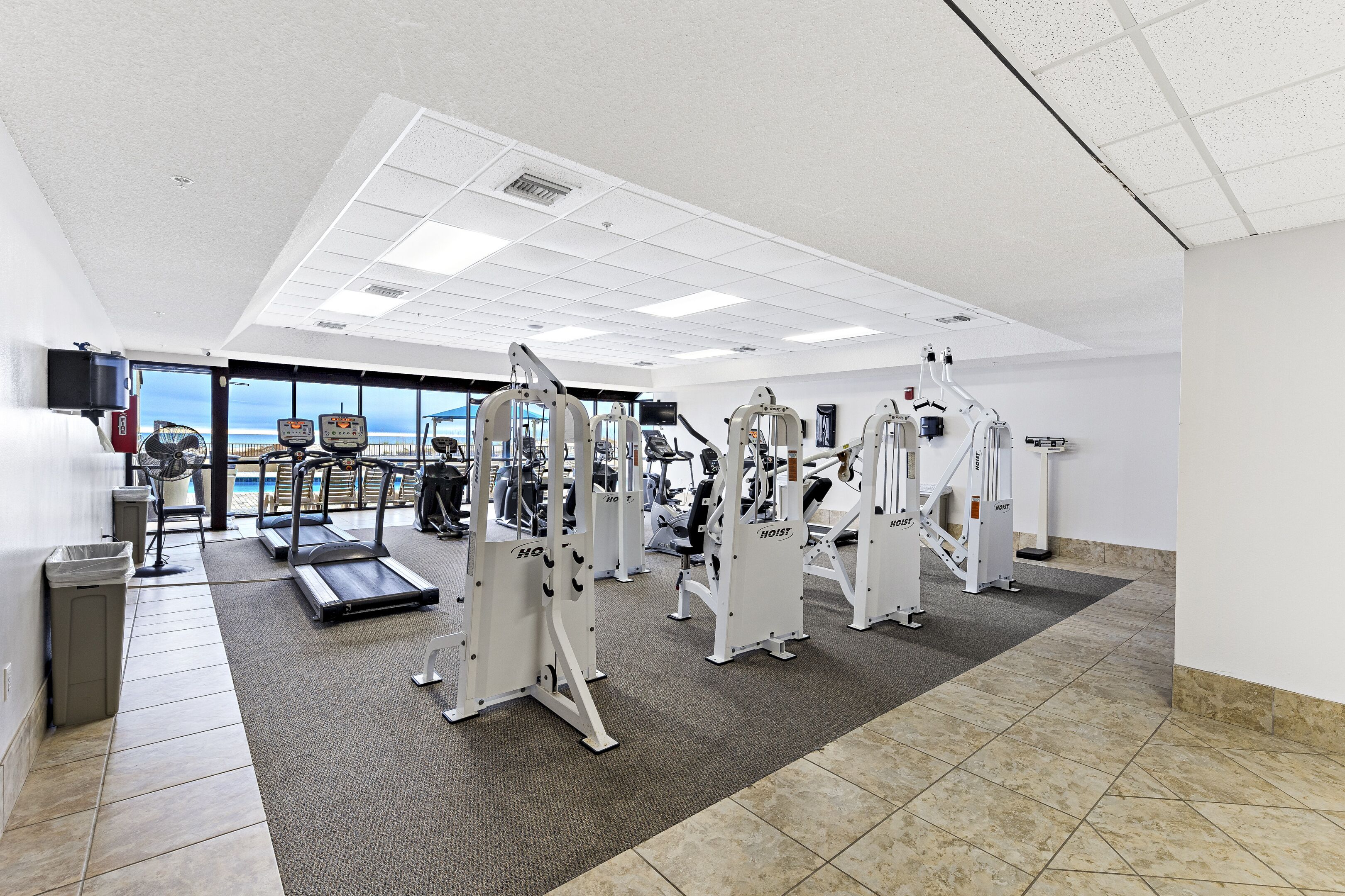 Ein Fitnessstudio mit Laufbändern, Kraftgeräten und Meerblick durch große Fenster.