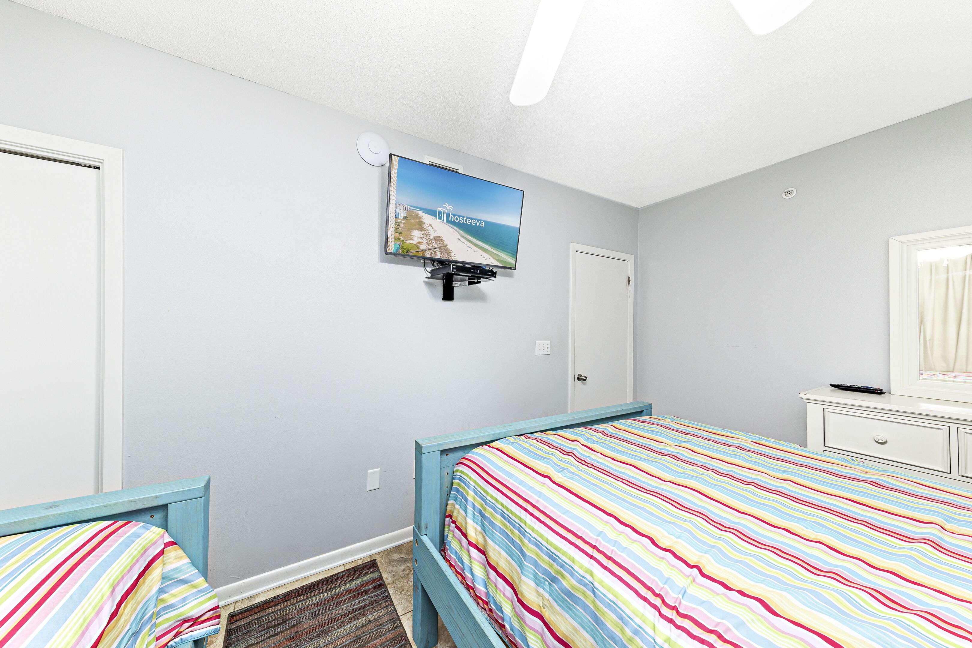 Un dormitorio con dos camas, un televisor montado en la pared y una ventana con cortinas.