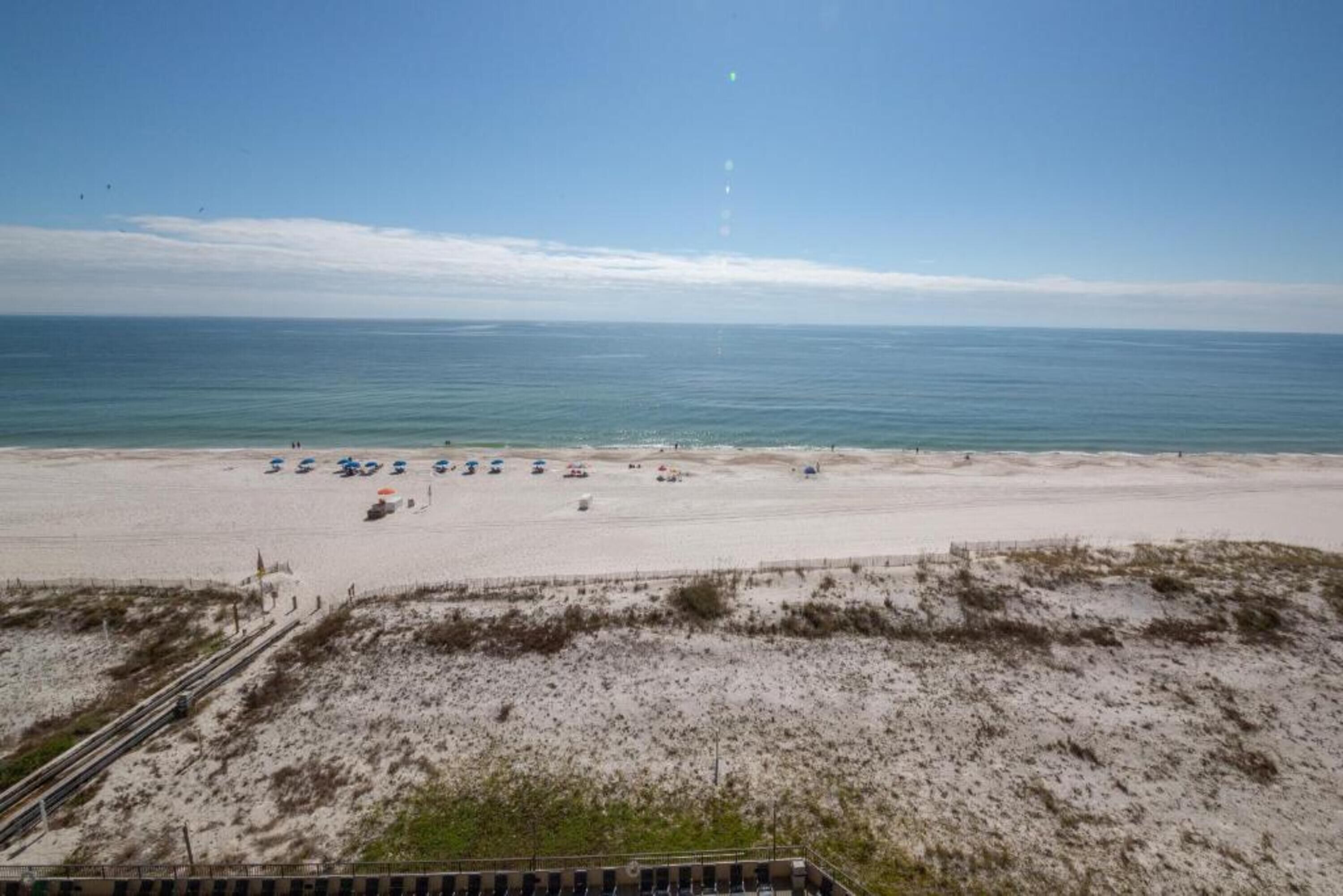 A beach with a sandy shore, a few umbrellas, and a clear sky.