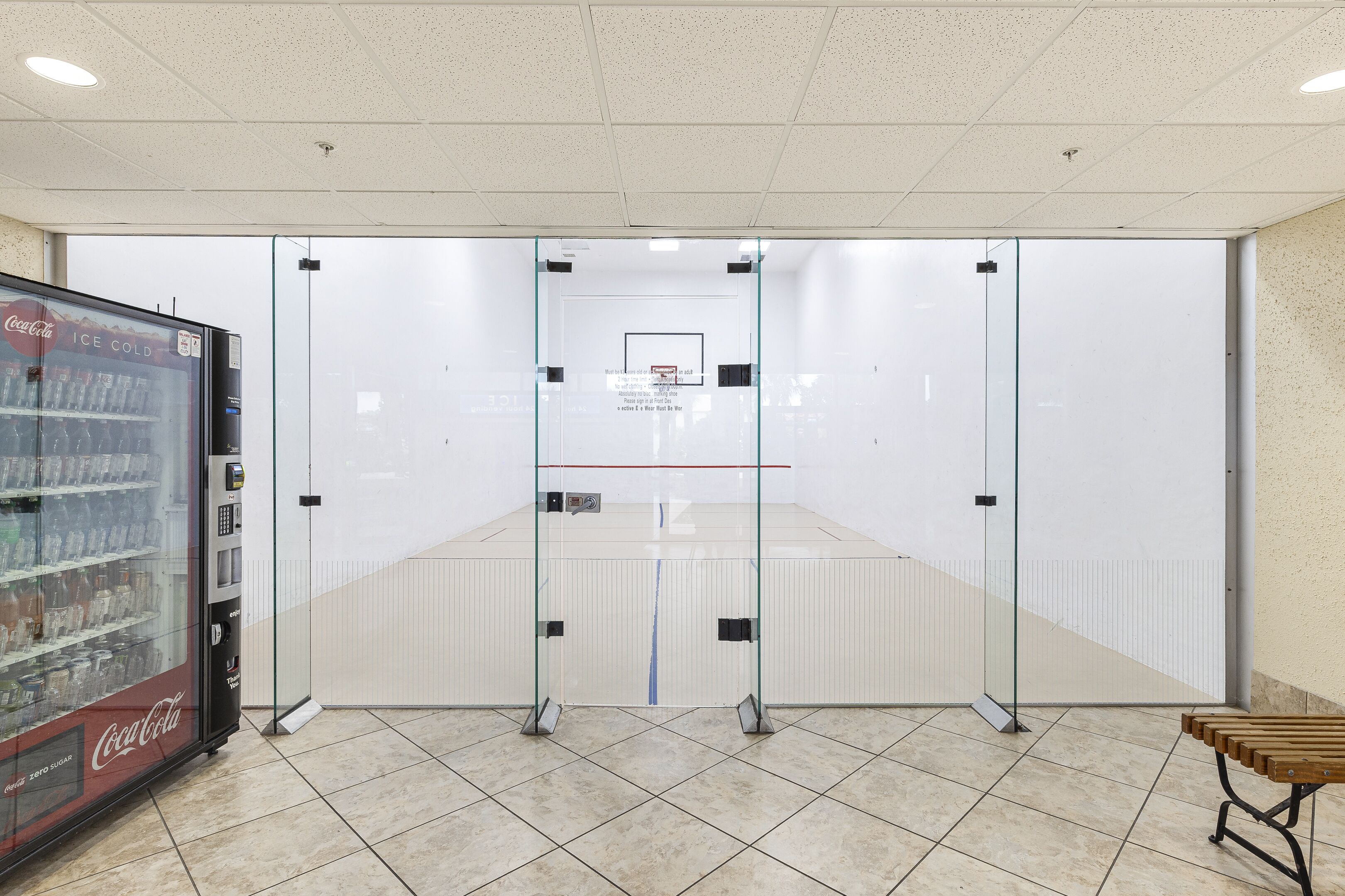 A clean, modern room with a glass partition, a Coca-Cola refrigerator, and a wooden bench.
