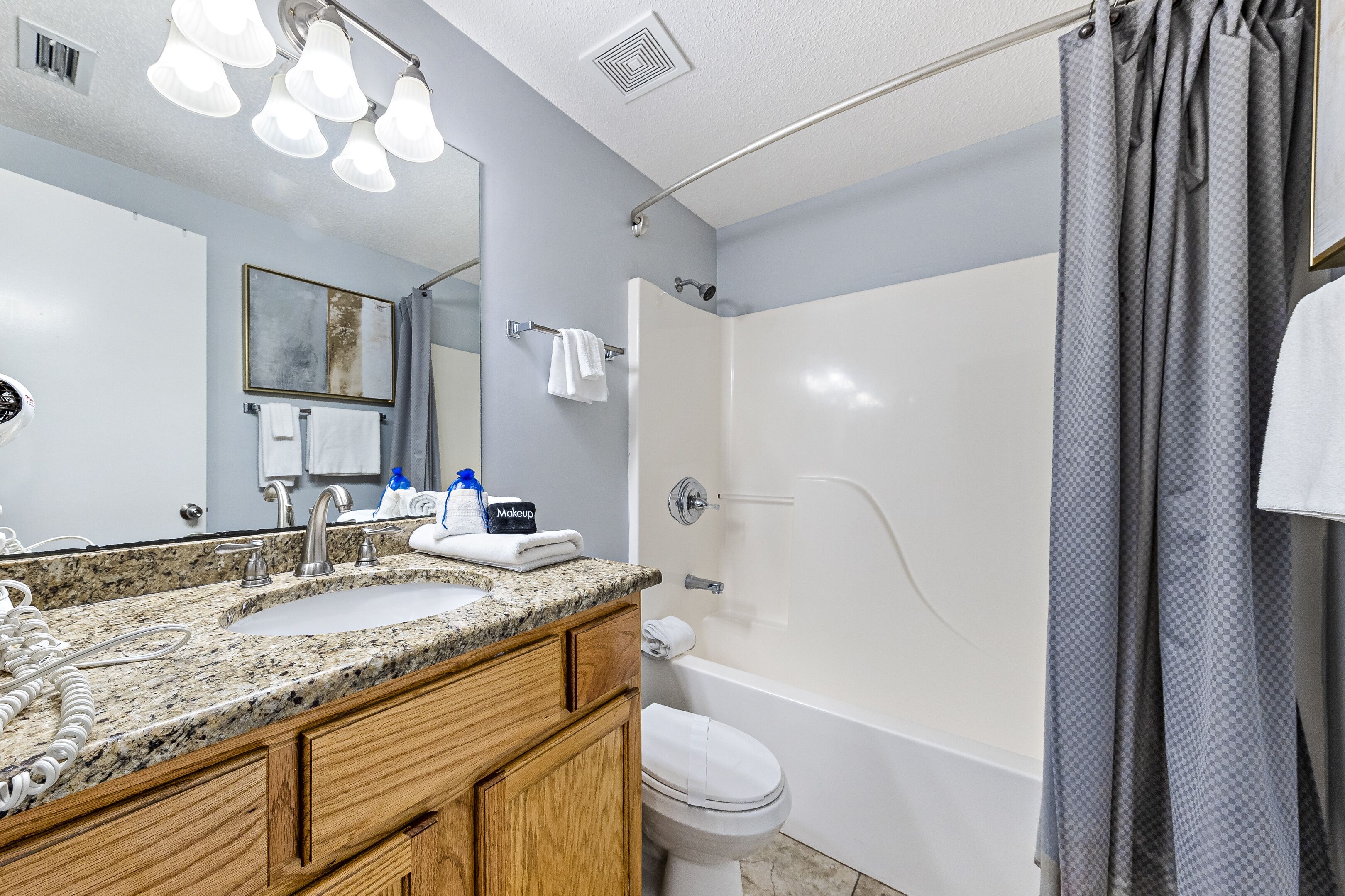 A bathroom with a granite countertop sink, a toilet, a bathtub, and a shower curtain.