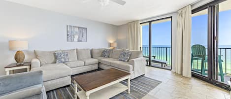 A living room with a sectional sofa, a coffee table, and a view of the ocean through large sliding glass doors.