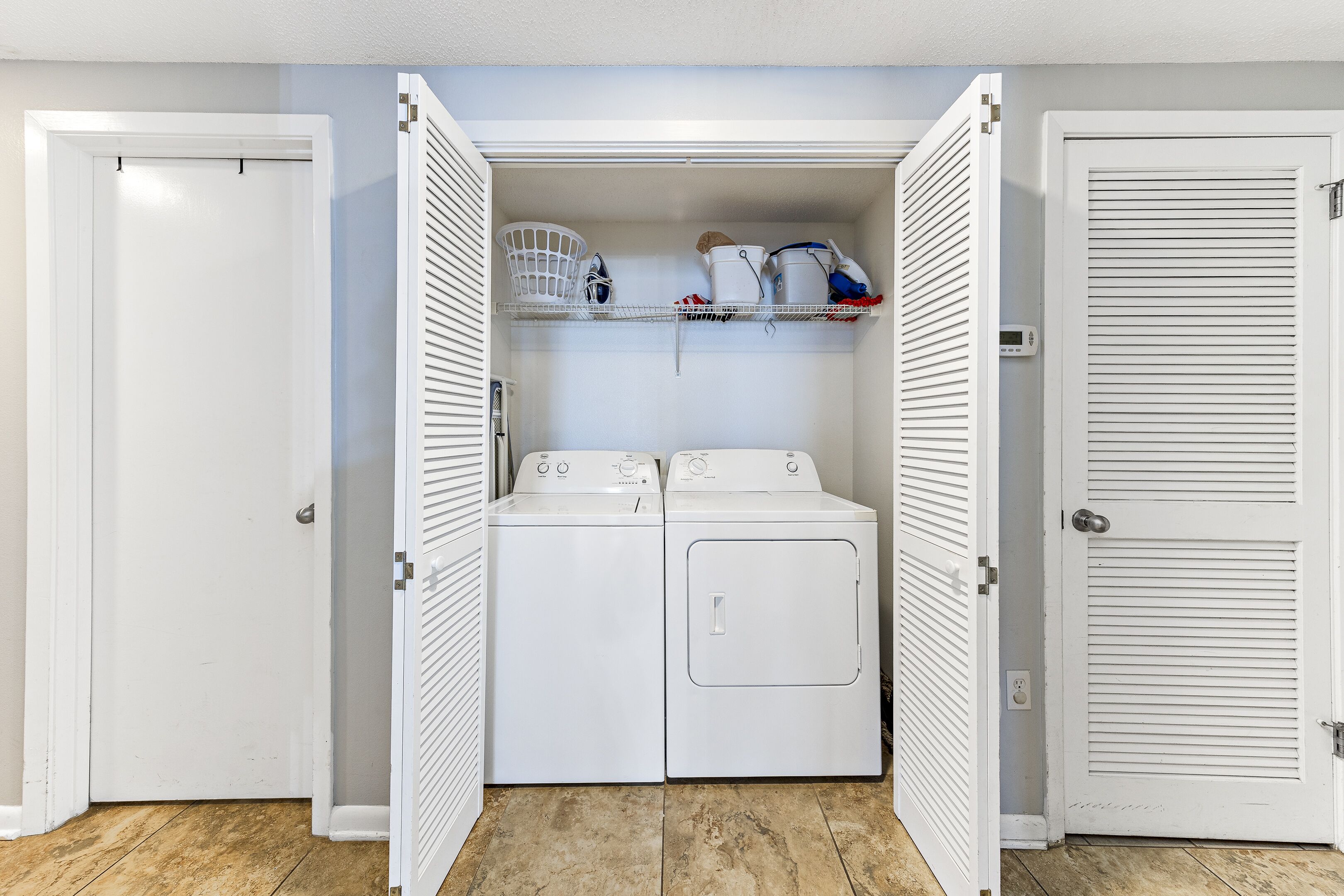 A laundry room with two washing machines, a dryer, and shelves above for storage.