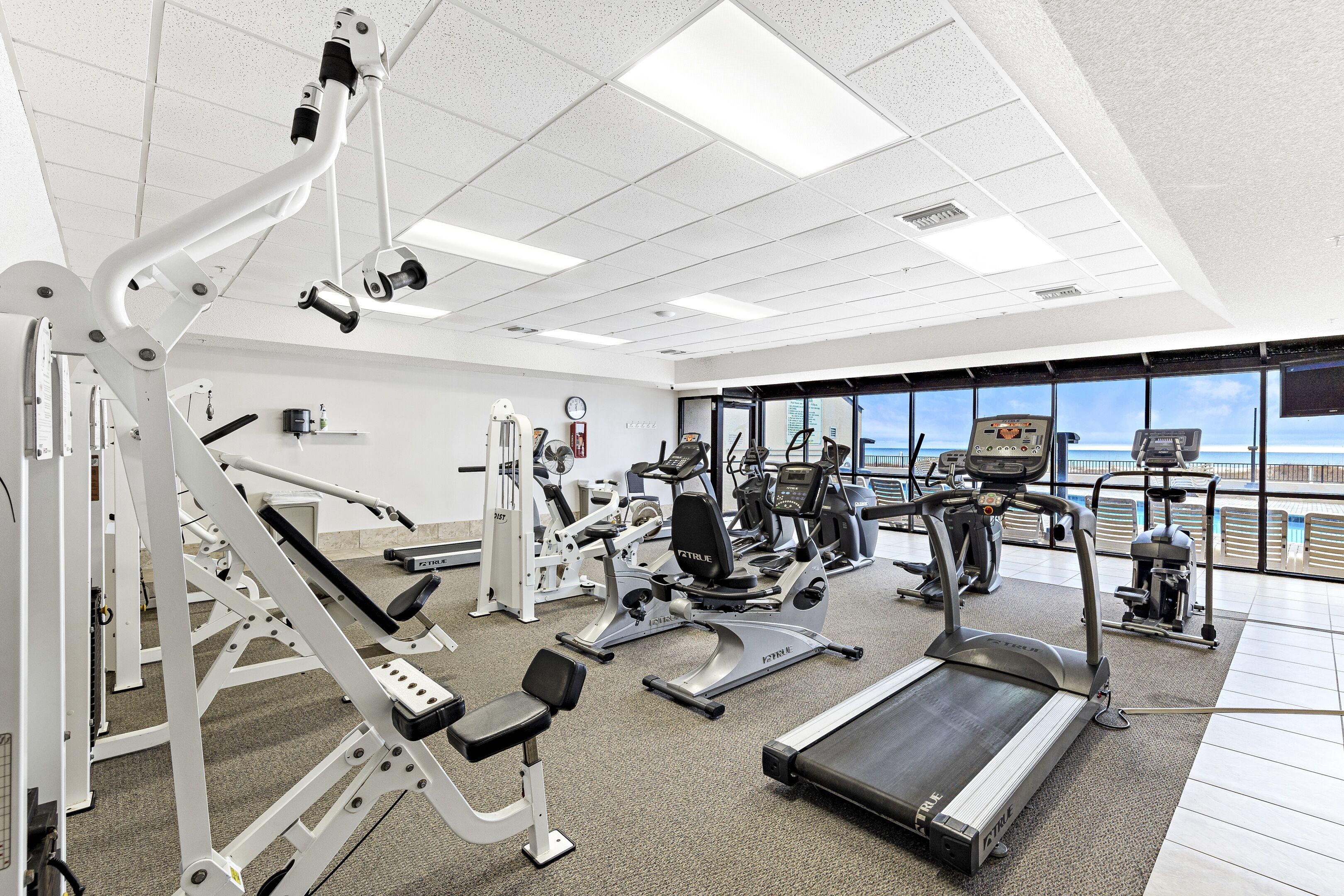 A gym with various exercise equipment, a treadmill, and large windows offering a view of the ocean.