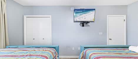A bedroom with two beds, a TV mounted on the wall, and a window with curtains.