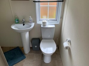 Un baño pequeño con un lavamanos, un inodoro y una ventana sobre el inodoro.