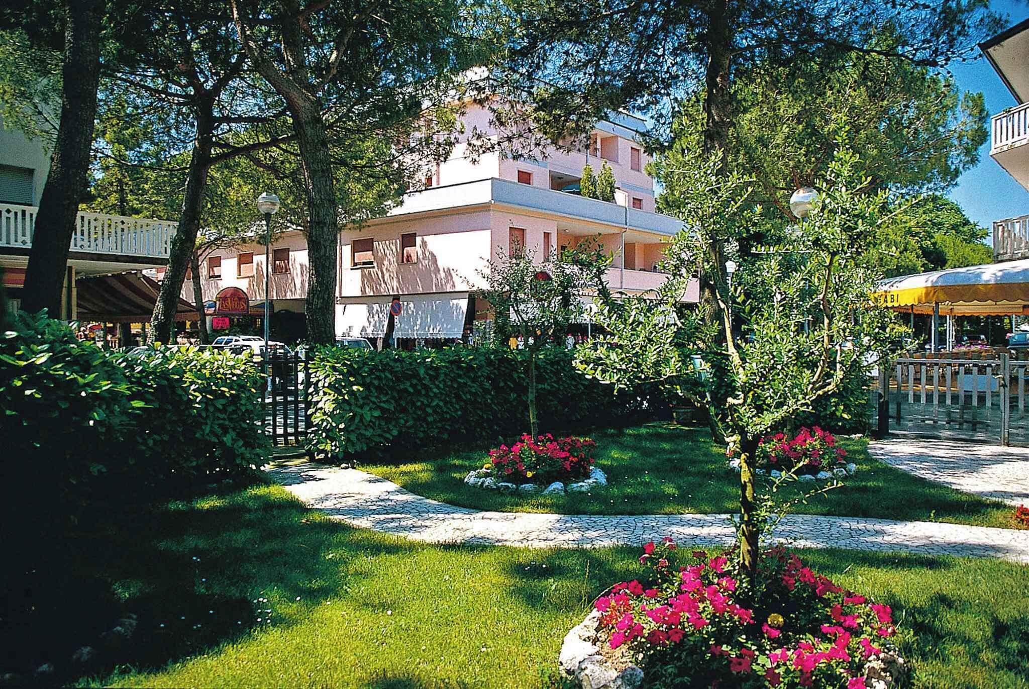 A garden with a pathway, a building with balconies, and a sign for a restaurant.