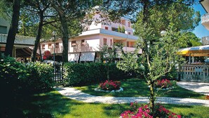 A garden with a pathway, a building with balconies, and a sign for a restaurant.