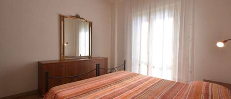 Un dormitorio con cama, cómoda, espejo y ventana con cortinas.