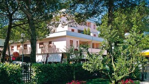 A multi-story building with balconies, surrounded by lush greenery and a small market area.