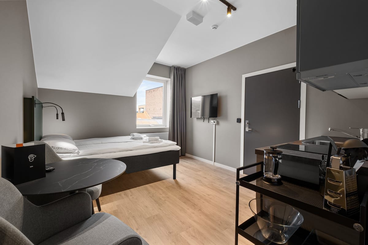 A modern room with a bed, a desk, a TV, and a kitchenette.