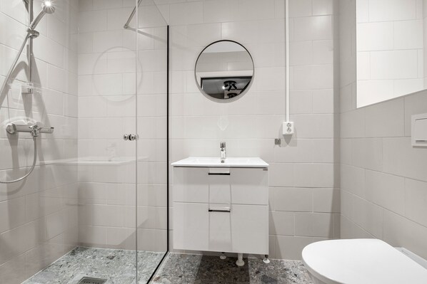 Un baño moderno con ducha envuelta en vidrio, un lavabo blanco con espejo y un inodoro.
