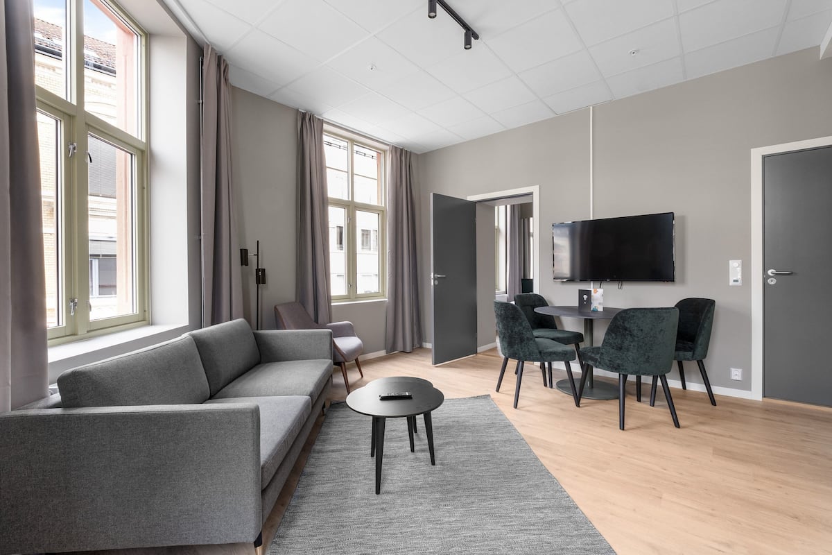 A modern living room with a grey sofa, a small round table, and a TV mounted on the wall.