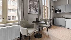 A modern kitchen with grey cabinets, a white refrigerator, and a microwave. There are two grey chairs and a small round table with a laptop. - Forenom Serviced Apartments Drammen (Drammen)