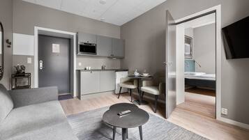 Una sala de estar moderna con un sofá gris, una mesita redonda y una cocina con gabinetes grises y un microondas.