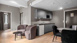 A modern kitchen with grey cabinets and a built-in oven. There are two grey armchairs and a black dining table with a black chair. - Forenom Serviced Apartments Drammen (Drammen)