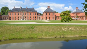 Ein großes, historisches Gebäude mit einer symmetrischen Fassade, zahlreichen Schornsteinen und einem zentralen Innenhof mit einem Teich.