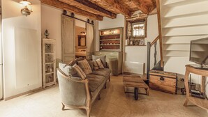 A rustic interior with a wooden ceiling, a sofa, a wooden chest, and a television on a wooden stand. - Les 3 Clefs de GaYa Well-being & private spa: swim spa, sauna, massage bed. (Saint-Jean-Ligoure)