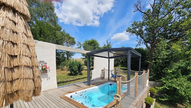 A wooden deck with a hot tub, a covered seating area, and a thatched roof structure. - Les 3 Clefs de GaYa Well-being & private spa: swim spa, sauna, massage bed. (Saint-Jean-Ligoure)