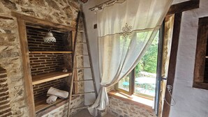 A rustic room with exposed brick walls, wooden shelves, a ladder, and a window with a curtain. - Les 3 Clefs de GaYa Well-being & private spa: swim spa, sauna, massage bed. (Saint-Jean-Ligoure)
