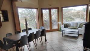 A dining area with a table and chairs, a sofa, and a view through large windows. - L'Escapade Ardéchoise (Fons)