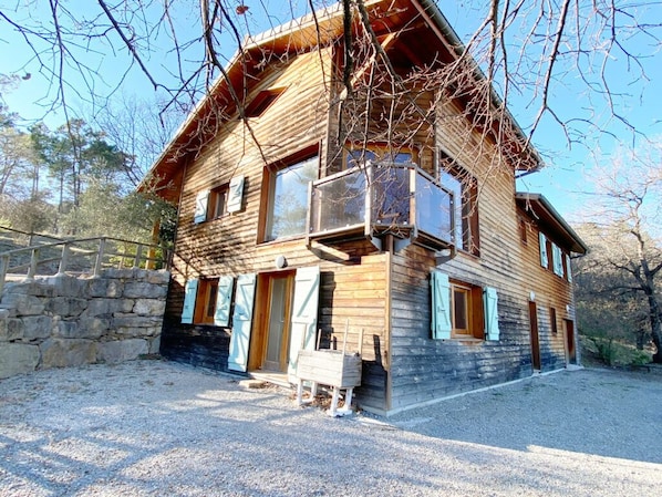 Une cabane en bois à deux étages, dotée d’un mur en pierre, d’un balcon et d’une allée gravillonnée.