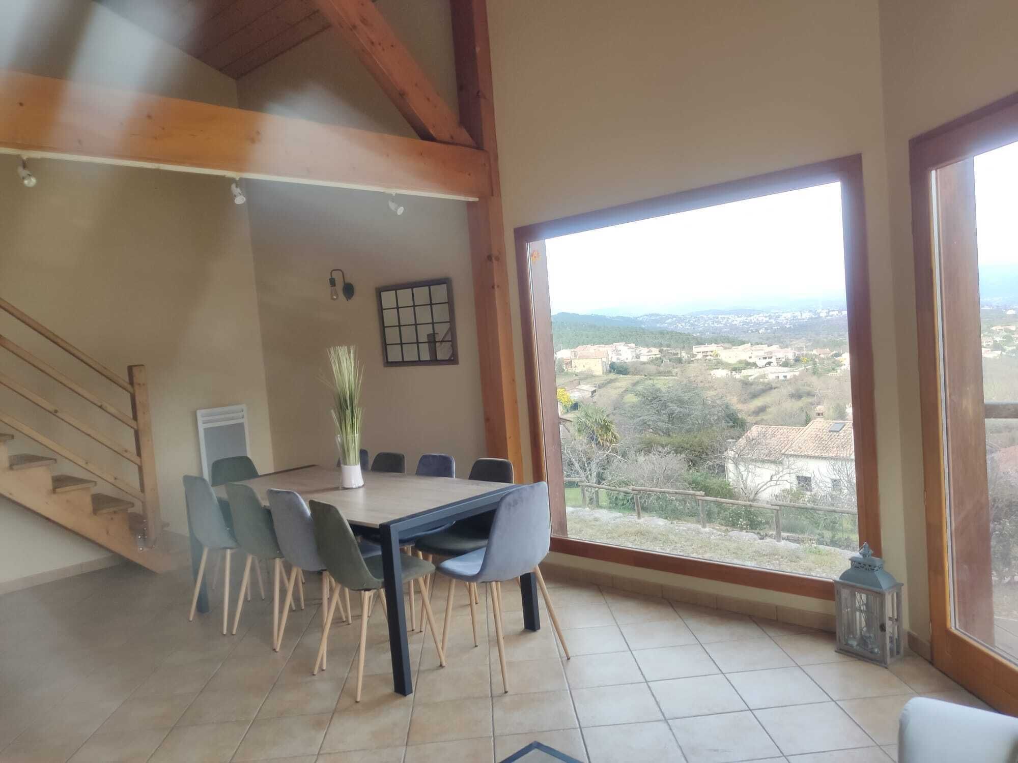 A dining area with a table and chairs, a view of a valley through large windows, and a staircase leading to an upper level.