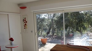 A room with a sliding glass door leading to a garden, a small round table with a vase, and a wooden bench. - Peace and relaxation in green Provence (Entrecasteaux)