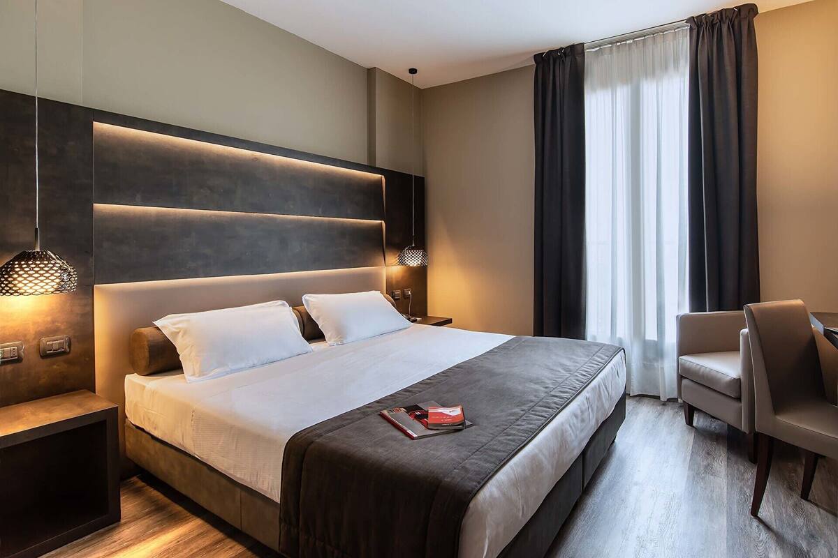 A modern hotel room with a large bed, bedside lamps, a desk, and a chair.